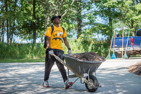A Lakeland University student smiles while pushing a full wheel barrel